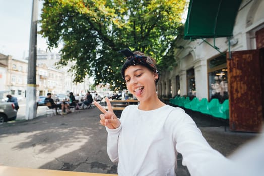 Close up portrait of a girl showing v-sign closing eyes showing tongue wear white t-shirt outdoor