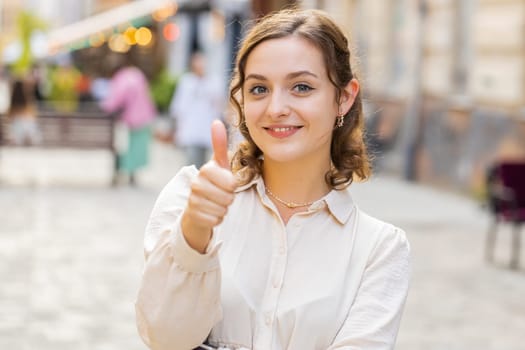 Like. Happy young pretty woman looking approvingly at camera showing thumbs up, like sign positive something good positive feedback. Lovely girl walking in urban city street. Town lifestyles outdoor