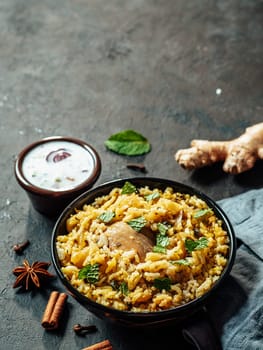 Pakistani food - biryani rice with chicken and raita yoghurt dip. Delicious hyberabadi chicken biryani on black background. Copy space for text. Vertical