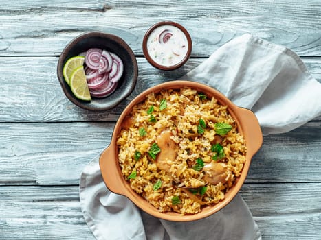 Pakistani food - biryani rice with chicken and raita yoghurt dip. Delicious hyberabadi chicken biryani on gray wooden background. Top view or flat lay. Copy space