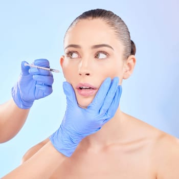 Face, beauty and woman with plastic surgeon or injection for transformation in studio with blue background. Girl, filler and skincare for cosmetic with collagen or fear for doctor hands with syringe