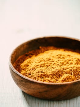 Indian or pakistani masala powder in small wooden bowl. Homemade dry curry garam masala mix spices blend on white wooden background with copy space. Vertical