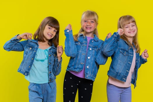 Excited happy teenage girls winning prize, celebrate birthday. Little child sisters celebrate success. Three siblings children kids becoming surprised about sudden dream come true on yellow background