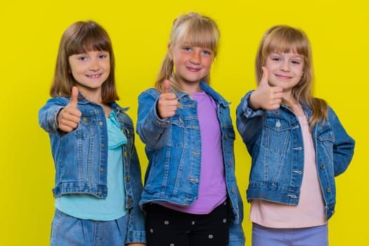 Like. Teenage girls raises thumbs up agrees, gives positive reply recommends advertisement likes good, nice feedback. Little children sisters. Three siblings kids isolated on studio yellow background