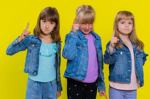 Quarrel. Displeased teenage girls gesturing hands with irritation and displeasure, blaming scolding for failure, asking why this happened. Children sisters. Three siblings kids on yellow background