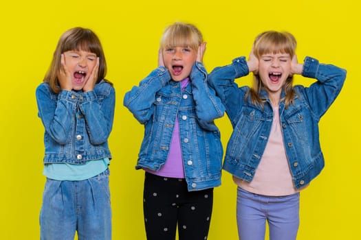 Teenage girls screams from stress tension problems feels horror hopelessness fear surprise shock expresses gestures rage. Children sisters. Three siblings kids isolated on studio yellow background
