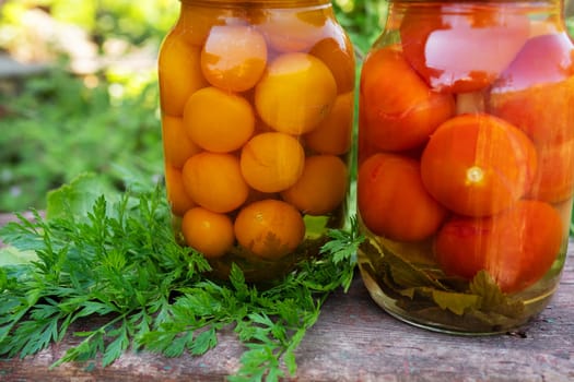 Tomatoes yellow and red in a jar, the process of harvesting for the winter. Close-up, jars outside on a wooden chair