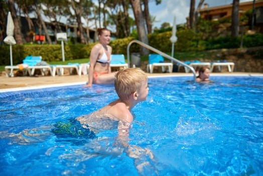 Young boy kid child eight years old splashing in swimming pool having fun leisure activity. Boy happy swimming in a pool. Activities on the pool, children swimming and playing in water, happiness and summertime