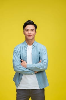 Confident young asian man standing cross arms against yellow background