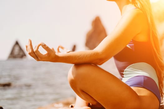 Yoga on the beach. A happy woman meditating in a yoga pose on the beach, surrounded by the ocean and rock mountains, promoting a healthy lifestyle outdoors in nature, and inspiring fitness concept