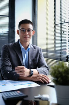 Portrait of successful businessman in smart suit sitting in modern workplace and looking at camera.