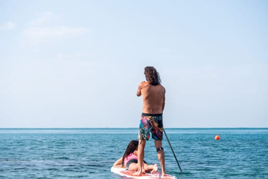 Silhouette of woman standing, surfing on SUP board, confident paddling through water surface. Idyllic sunset or sunrise. Sports active lifestyle at sea or river.