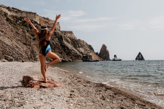 Woman sea yoga. Back view of free calm happy satisfied woman with long hair standing on top rock with yoga position against of sky by the sea. Healthy lifestyle outdoors in nature, fitness concept.