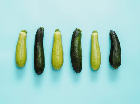 Row of green and dark zucchini on blue plain background