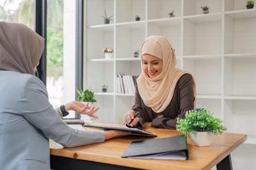Young muslim female business worker discussing with friends sitting together, working with tablet and financial documents at desk.