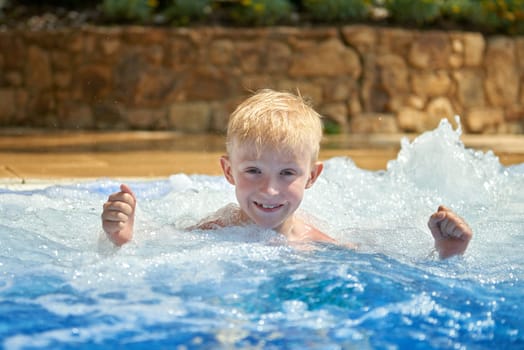 Young boy kid child eight years old splashing in swimming pool having fun leisure activity. Boy happy swimming in a pool. Activities on the pool, children swimming and playing in water, happiness and summertime