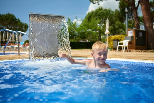 Young boy kid child eight years old splashing in swimming pool having fun leisure activity. Boy happy swimming in a pool. Activities on the pool, children swimming and playing in water, happiness and summertime