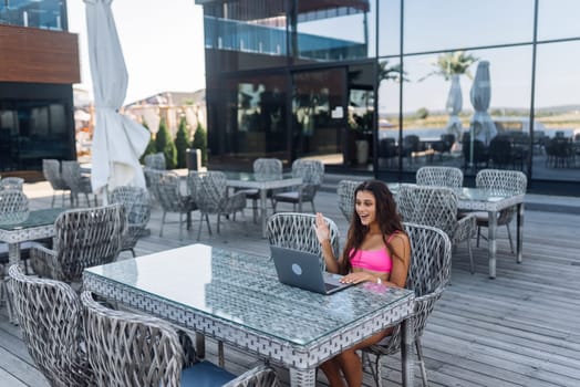 Cute young woman sitting on terrace, while using laptop for work at summer day