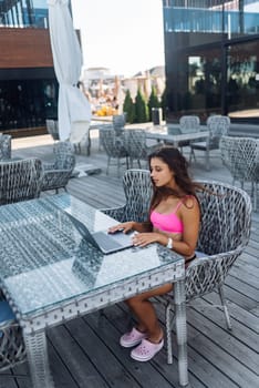 Cute young woman sitting on terrace, while using laptop for work at summer day