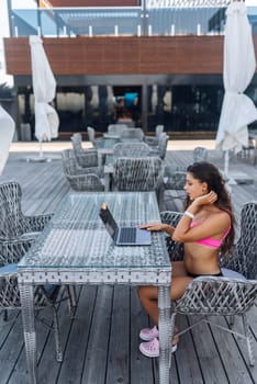 Cute young woman sitting on terrace, while using laptop for work at summer day