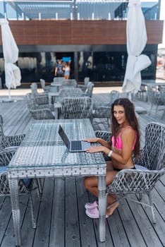 Cute young woman sitting on terrace, while using laptop for work at summer day