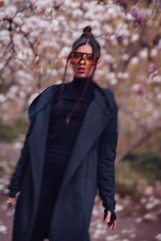 Beautiful dramatic young woman wearing black kimono and yellow glasses with cherry blossoms, sakura view. High quality photo