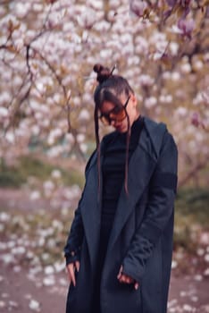 Beautiful dramatic young woman wearing black kimono and yellow glasses with cherry blossoms, sakura view. High quality photo