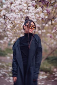 Beautiful dramatic young woman wearing black kimono and yellow glasses with cherry blossoms, sakura view. High quality photo