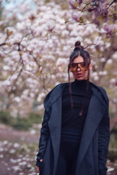 Beautiful dramatic young woman wearing black kimono and yellow glasses with cherry blossoms, sakura view. High quality photo