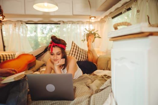 Portrait of a cute lesbian couple. Two girls spend time tenderly together watching movie on laptop in a camper trailer with LGBT flag on the wall. Love and attitude. LGBT concept. High quality photo