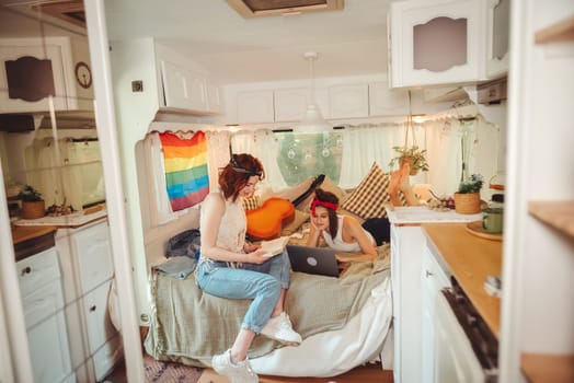 Portrait of a cute lesbian couple. Two girls spend time tenderly together watching movie on laptop in a camper trailer with LGBT flag on the wall. Love and attitude. LGBT concept. High quality photo