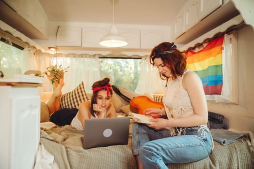 Portrait of a cute lesbian couple. Two girls spend time tenderly together watching movie on laptop in a camper trailer with LGBT flag on the wall. Love and attitude. LGBT concept. High quality photo