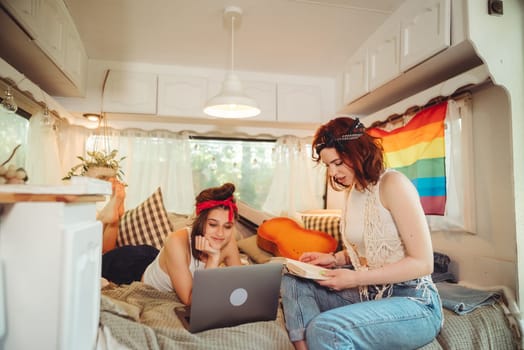 Portrait of a cute lesbian couple. Two girls spend time tenderly together watching movie on laptop in a camper trailer with LGBT flag on the wall. Love and attitude. LGBT concept. High quality photo