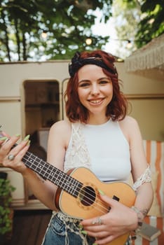 Happy hippie girl are having a good time with playing on guitar in camper trailer. Holiday, vacation, trip concept.High quality photo