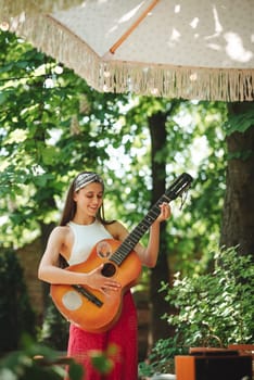 Happy hippie girl is having a good time with playing on guitar in camper trailer. Holiday, vacation, trip concept.High quality photo