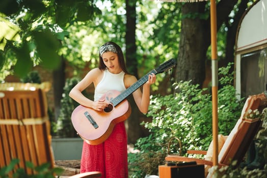 Happy hippie girl is having a good time with playing on guitar in camper trailer. Holiday, vacation, trip concept.High quality photo