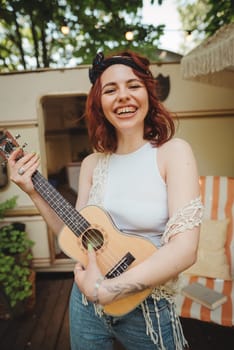 Happy hippie girl are having a good time with playing on guitar in camper trailer. Holiday, vacation, trip concept.High quality photo