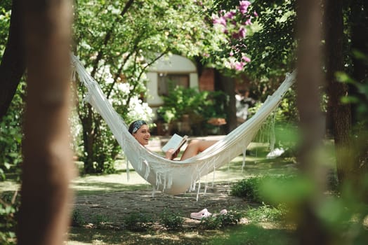 Happy hippie girl is reading a book in hammock having a good time with playing in camper trailer. Holiday, vacation, trip concept.High quality photo