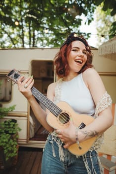 Happy hippie girl are having a good time with playing on guitar in camper trailer. Holiday, vacation, trip concept.High quality photo