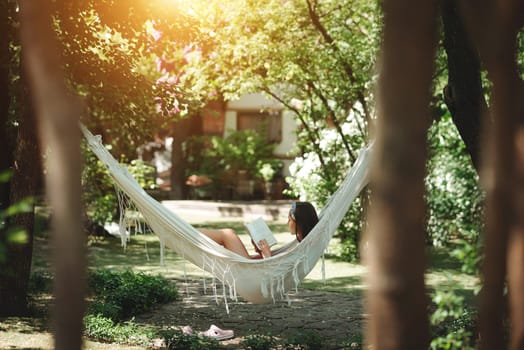 Happy hippie girl is reading a book in hammock having a good time with playing in camper trailer. Holiday, vacation, trip concept.High quality photo