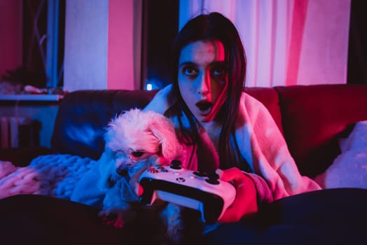 Close up portrait of A gamer or a streamer girl at home in a dark room with a game controller playing with her dog and sits in front of a monitor or TV. Crazy emotions. High quality photo