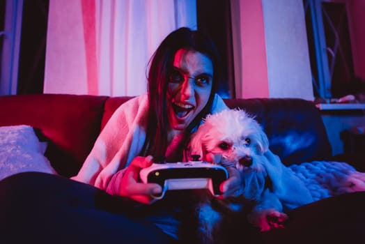 Close up portrait of A gamer or a streamer girl at home in a dark room with a game controller playing with her dog and sits in front of a monitor or TV. Crazy emotions. High quality photo