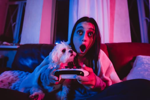 Close up portrait of A gamer or a streamer girl at home in a dark room with a game controller playing with her dog and sits in front of a monitor or TV. Crazy emotions. High quality photo