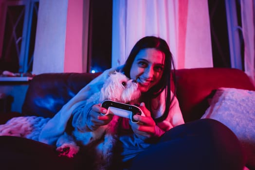 Close up portrait of A gamer or a streamer girl at home in a dark room with a game controller playing with her dog and sits in front of a monitor or TV. Crazy emotions. High quality photo