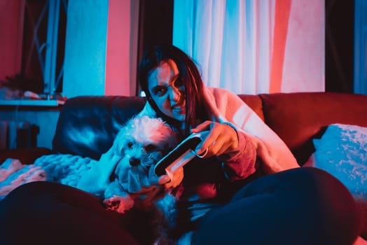 Close up portrait of A gamer or a streamer girl at home in a dark room with a game controller playing with her dog and sits in front of a monitor or TV. Crazy emotions. High quality photo