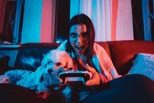 Close up portrait of A gamer or a streamer girl at home in a dark room with a game controller playing with her dog and sits in front of a monitor or TV. Crazy emotions. High quality photo