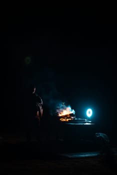 Man preparing bbq grill to cook on fire. Outside dark shot. Freeze moment of fire. High quality photo