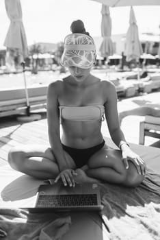 beautiful girl in bikini is typing on a laptop and sunbathing on the beach. High quality photo Black and white photo