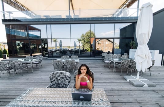 Cute young woman sitting on terrace, while using laptop for work at summer day