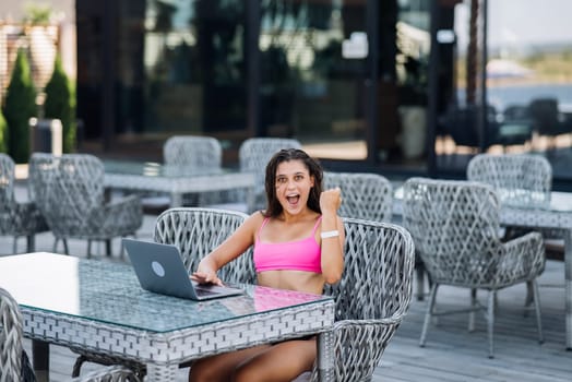Cute young woman sitting on terrace, happy with hands up winner at summer day